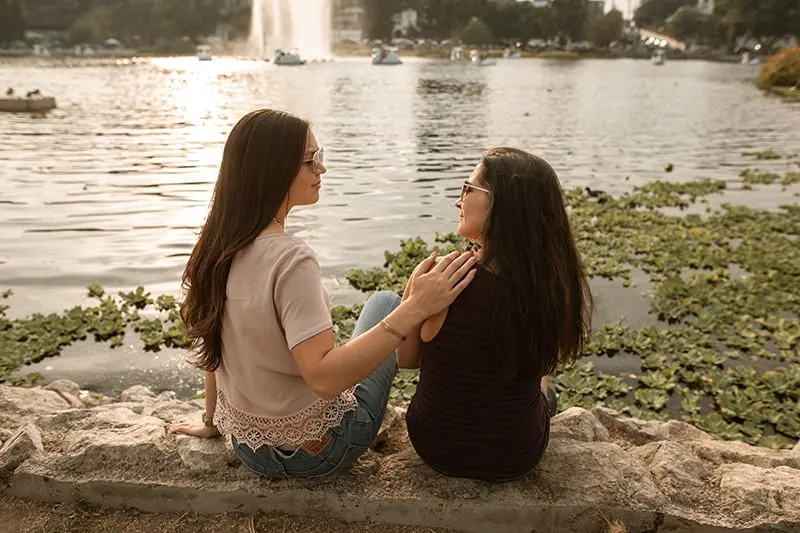 Eine Frau berührt die Schulter ihrer Freundin, während sie in der Nähe des Sees spricht