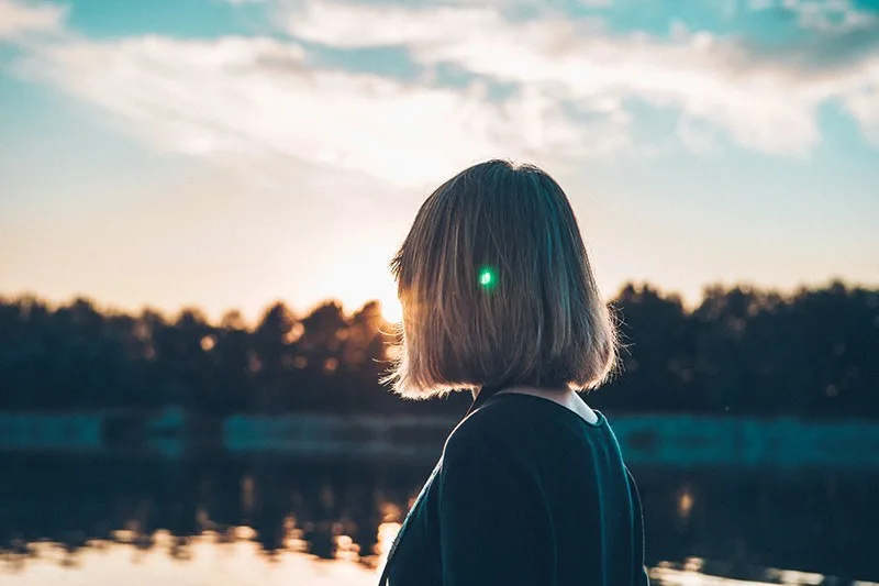 eine Frau, die den Sonnenuntergang beobachtet, während sie in der Nähe des Sees steht