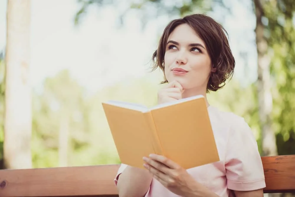 eine Frau, die draußen mit einem Buch in der Hand sitzt und positiv denkt