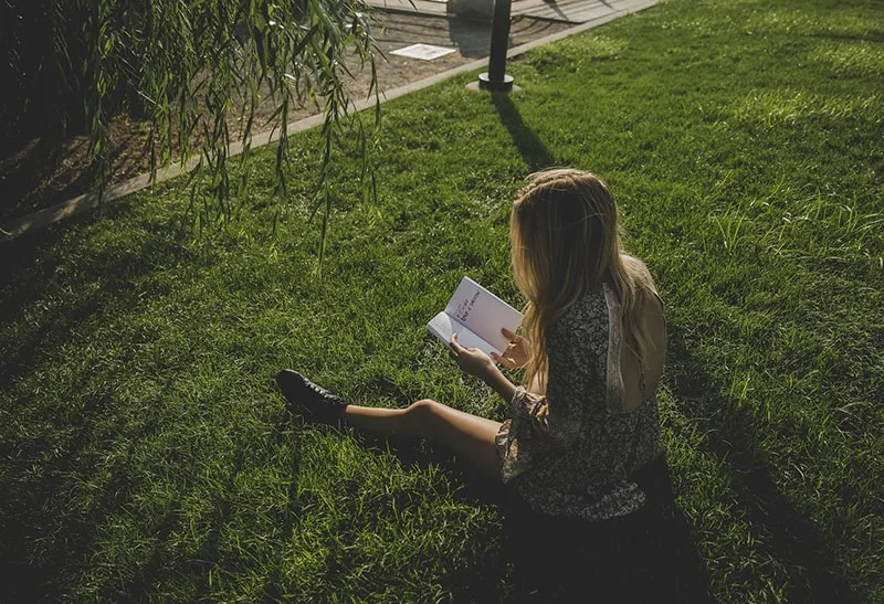 eine Frau, die ein Buch liest, das auf dem Gras sitzt