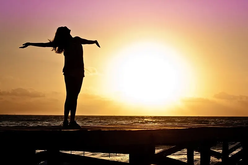 eine Frau, die ihre Arme hebt und während eines Sonnenuntergangs in den Himmel schaut
