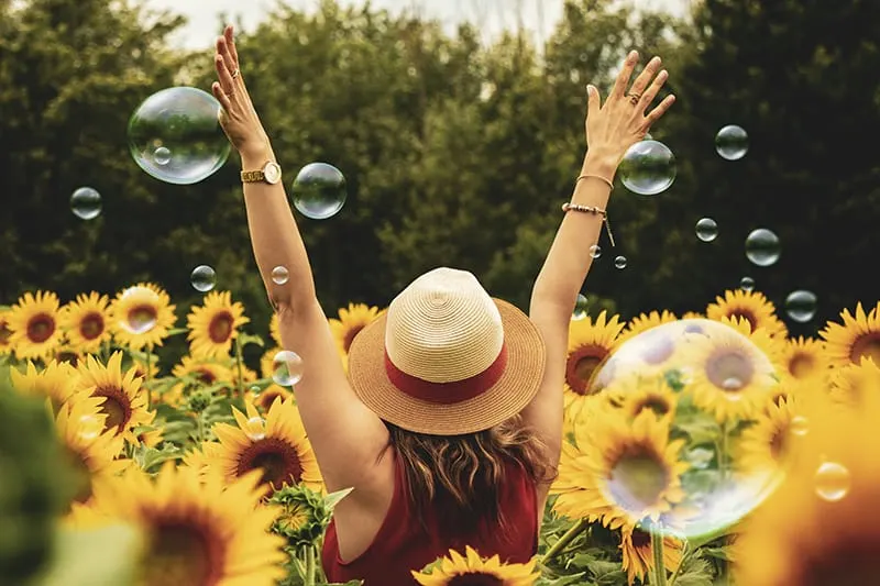 eine Frau, die im Sonnenblumenfeld steht und ihre Hände hebt