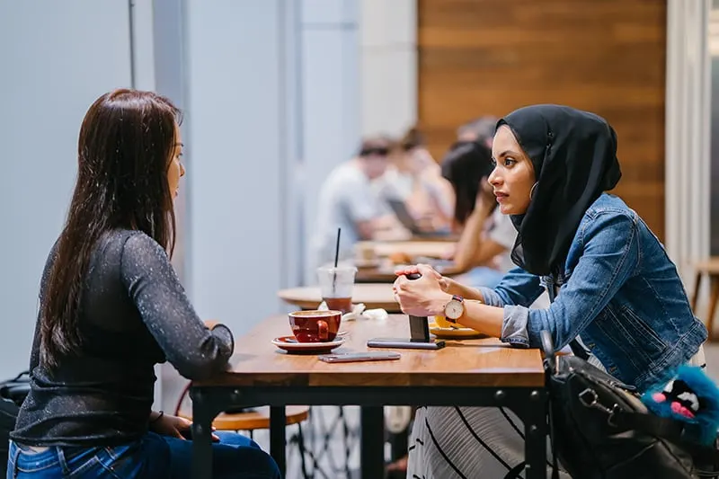 eine Frau in einer Jeansjacke, die ihrer Freundin gesteht, während sie im Café sitzt