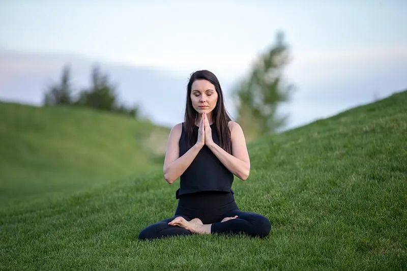 eine Frau, die meditiert, während sie tagsüber im Gras sitzt