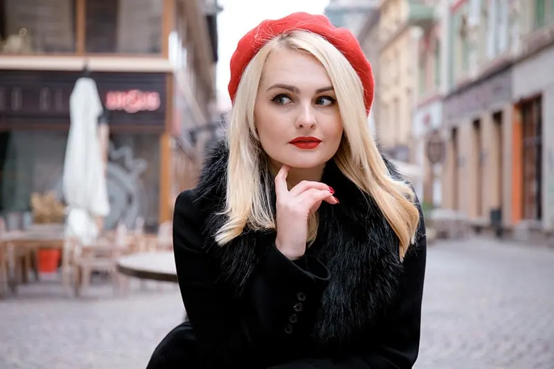 eine Frau mit einem roten Hut, der beiseite schaut und nachdenklich aussieht, während sie auf der Straße steht