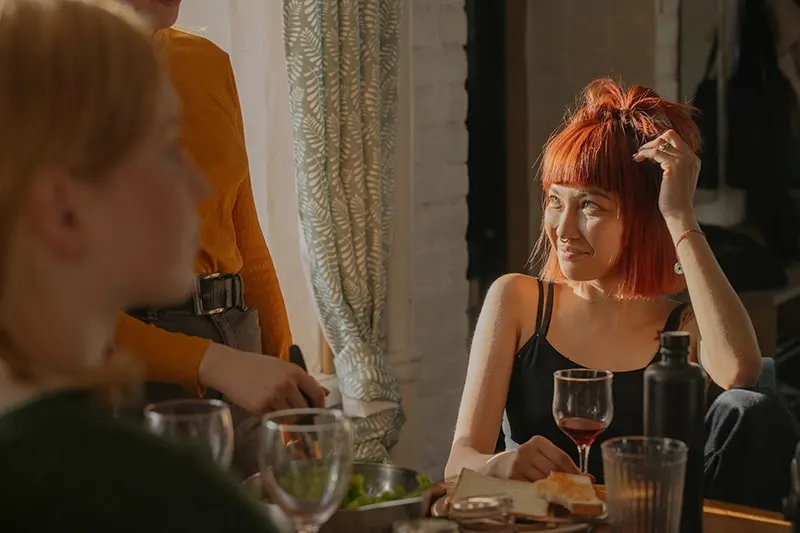 eine Frau mit roten Haaren, die Freunde beim Sitzen am Tisch ansieht