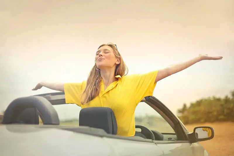 Eine Frau sitzt im Auto und breitet die Arme aus, während sie zum Himmel schaut