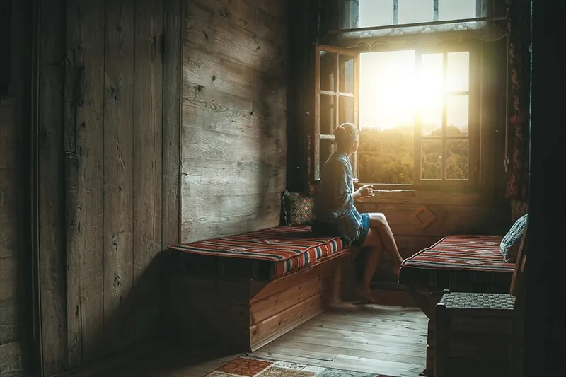 eine Frau, die neben einem Fenster sitzt und morgens den Sonnenaufgang beobachtet