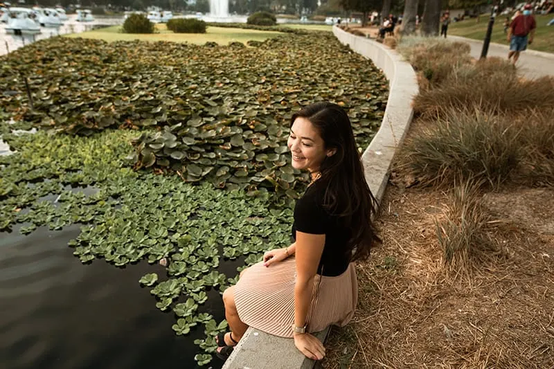 eine lächelnde Frau, die allein in der Nähe des Sees im Park sitzt