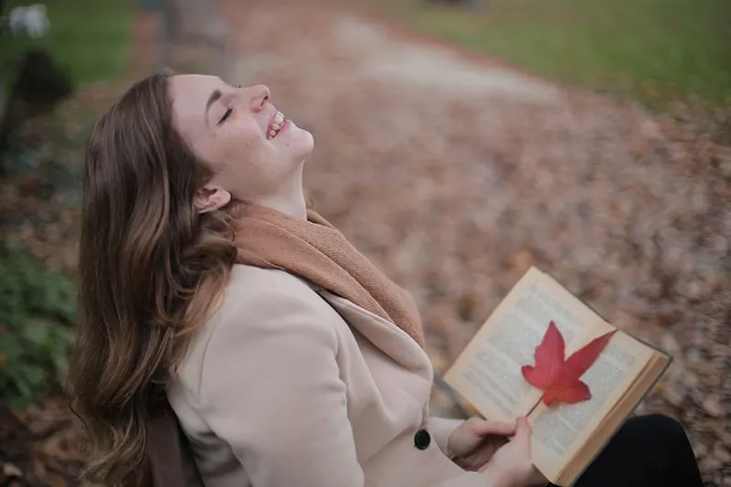 eine lächelnde Frau, die ein Buch hält, während sie im Park sitzt