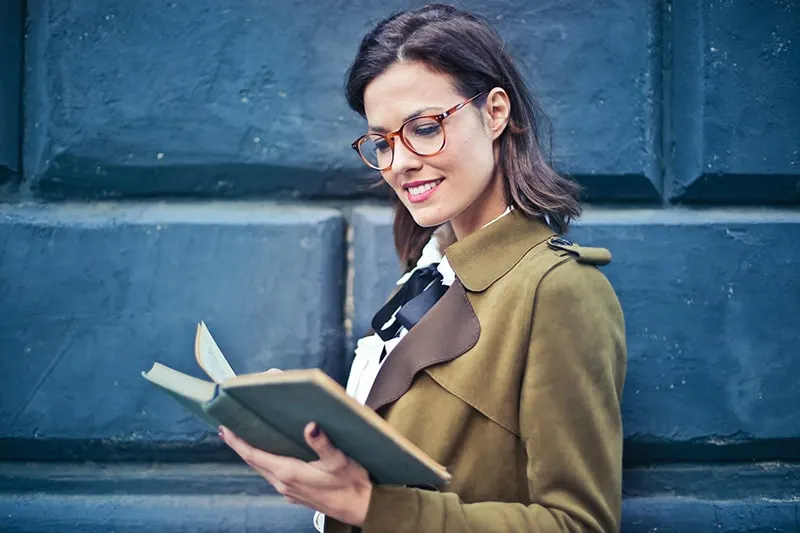eine lächelnde Frau, die ein Buch liest, das nahe der blauen Wand steht