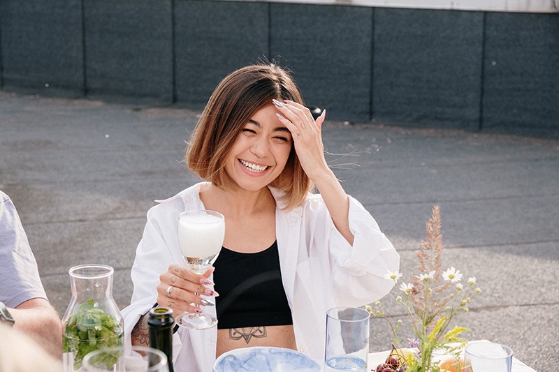 eine lächelnde Frau, die ein Glas Champagner hält, während sie auf einer Geburtstagsfeier am Tisch sitzt