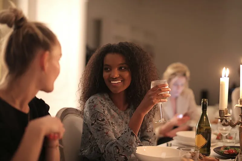 eine lächelnde Frau, die ein Glas Wein hält, während sie mit einer Freundin spricht