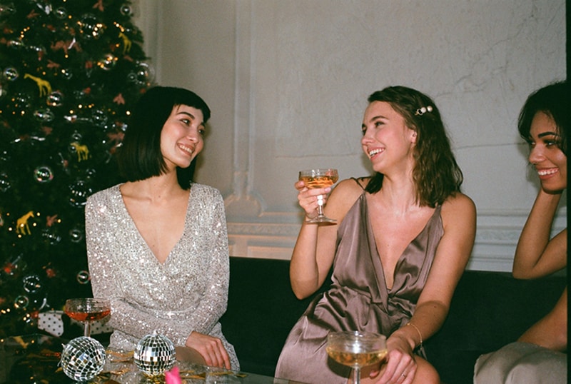 eine lächelnde Frau, die ein Glas mit Getränk hält, während sie mit Freunden sitzt