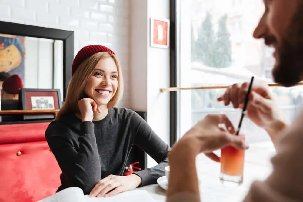 eine lächelnde Frau mit einer roten Mütze, die mit einem Mann in einem Café spricht