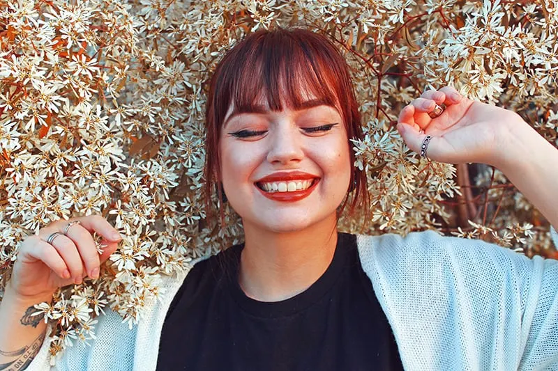 eine lächelnde Frau mit geschlossenen Augen, umgeben von Blumen
