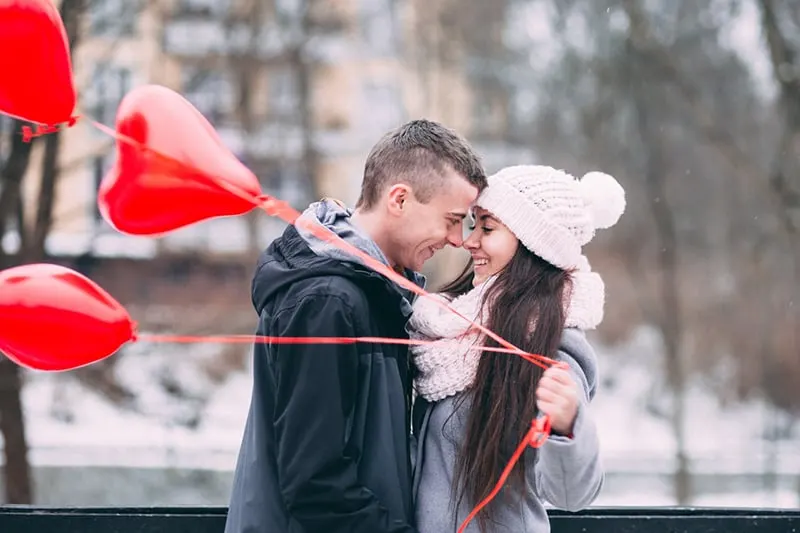 glückliches Paar einander gegenüber während die Frau rote Luftballons hält