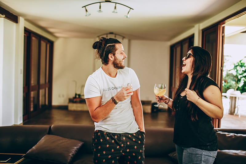 lächelnder Mann und eine Frau, die Getränke hält, während sie im Wohnzimmer sprechen