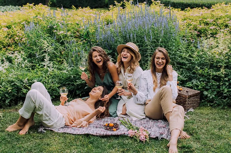 vier lachende Frauen sitzen im Gras und trinken Wein