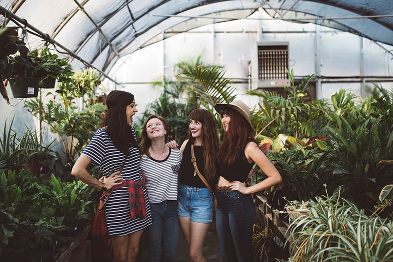 vier lachende Freundinnen, die sich im Gewächshaus umarmen