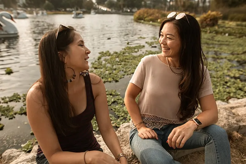 zwei Frauen lächeln und sprechen, während sie in der Nähe des Sees sitzen