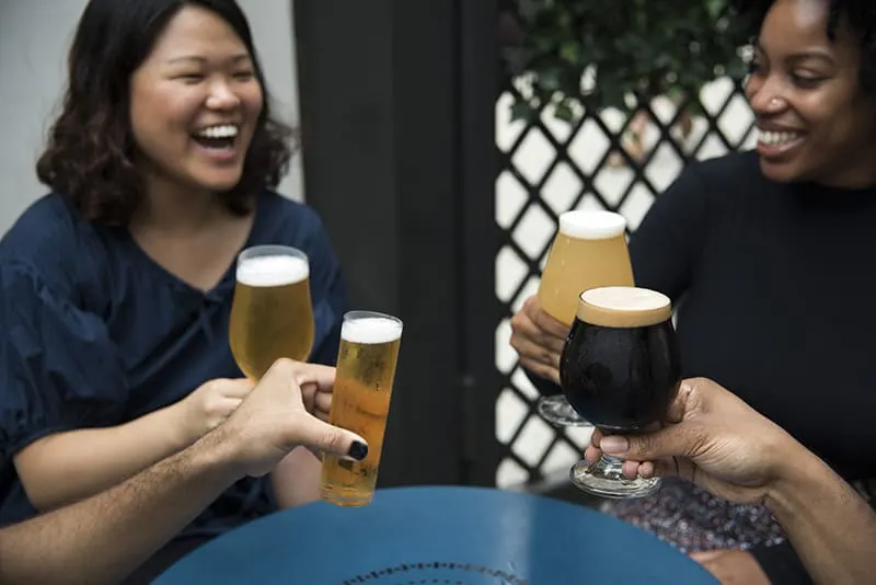 zwei Frauen lachen beim Anstoßen mit Freunden auf ein Bier