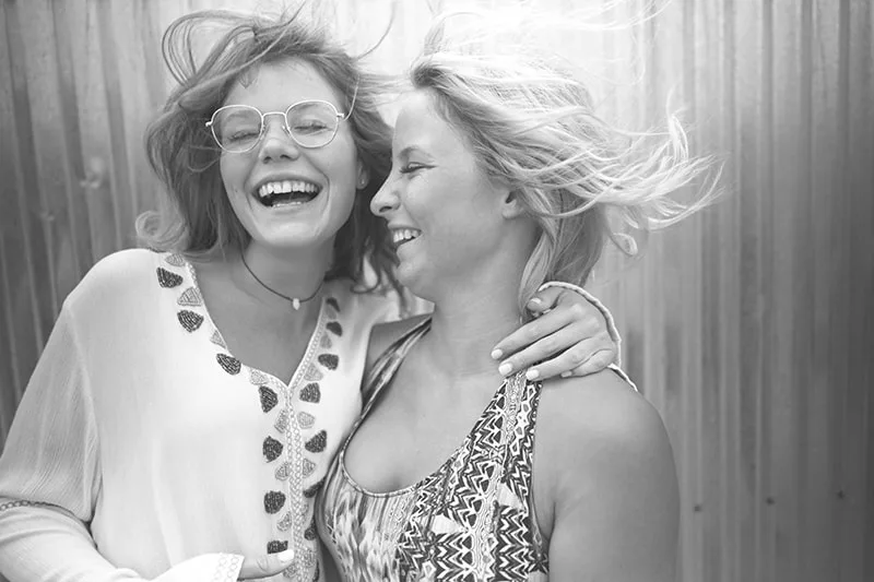 Zwei Frauen umarmen sich und lachen mit geschlossenen Augen
