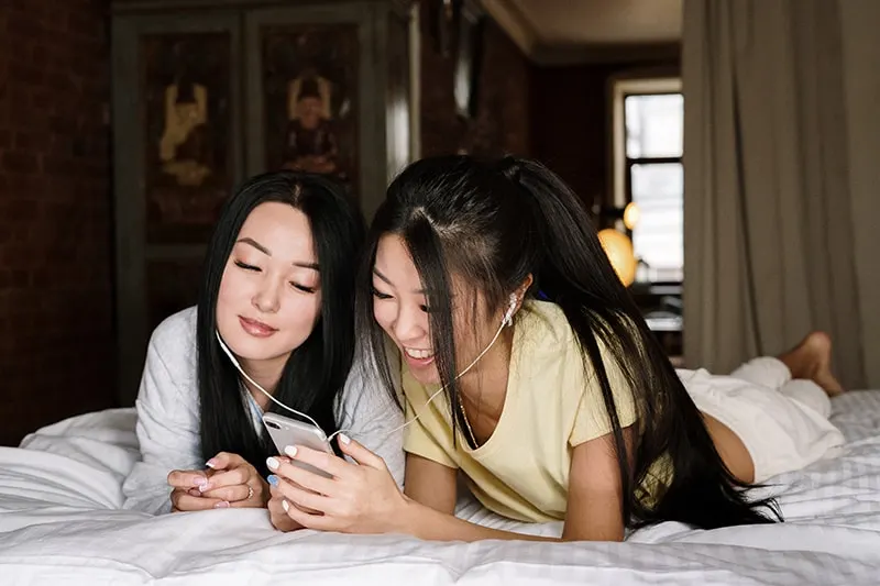 zwei Freundinnen hören zusammen Musik, während sie auf dem Bett liegen