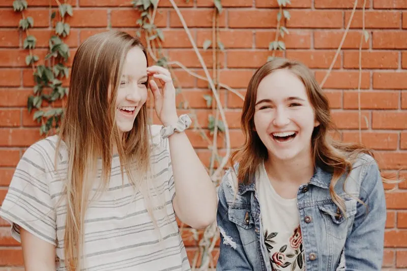zwei Mädchen, die zusammen lachen, stehen nahe der Mauer