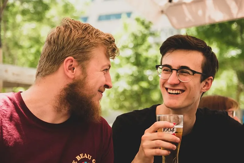 zwei lächelnde Freunde, die sich beim Biertrinken ansehen