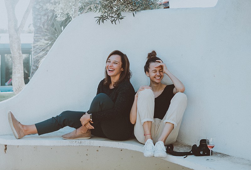 zwei lächelnde Freundinnen, die auf der weißen Bank sitzen