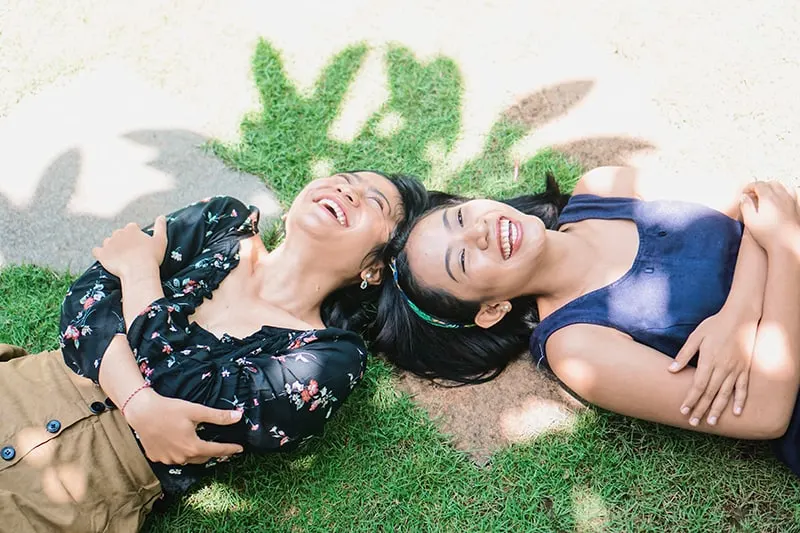 zwei lachende Frauen, die auf dem grünen Gras liegen