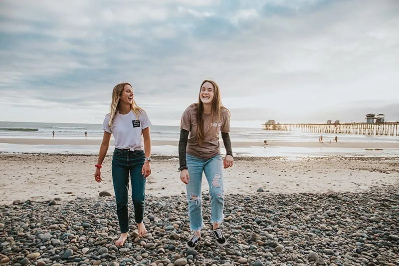 zwei lachende Freundinnen, die nahe dem Strand gehen
