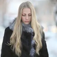 Auf der Straße im Schnee steht eine traurige Blondine in einem Mantel