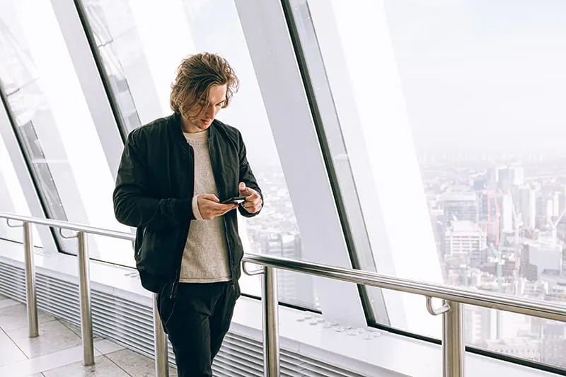 Ein Mann benutzt sein Smartphone, während er in der Nähe des großen Fensters geht