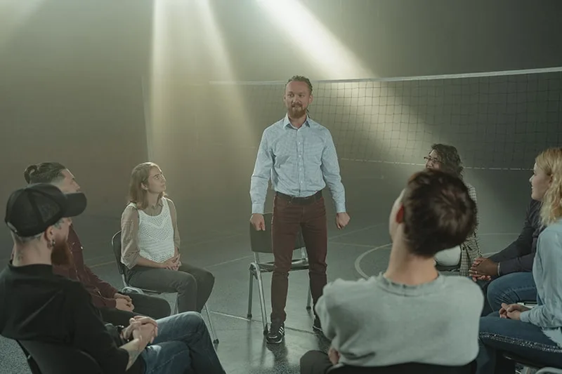 Ein Mann, der vor einer Gruppe von Menschen steht, die auf Stühlen sitzen
