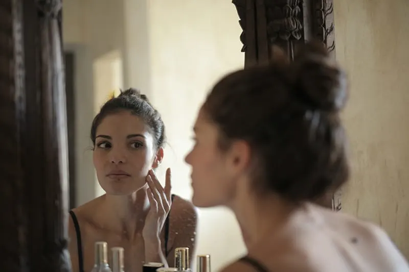 Frau berührt ihre Wange und schaut sich in den Spiegel