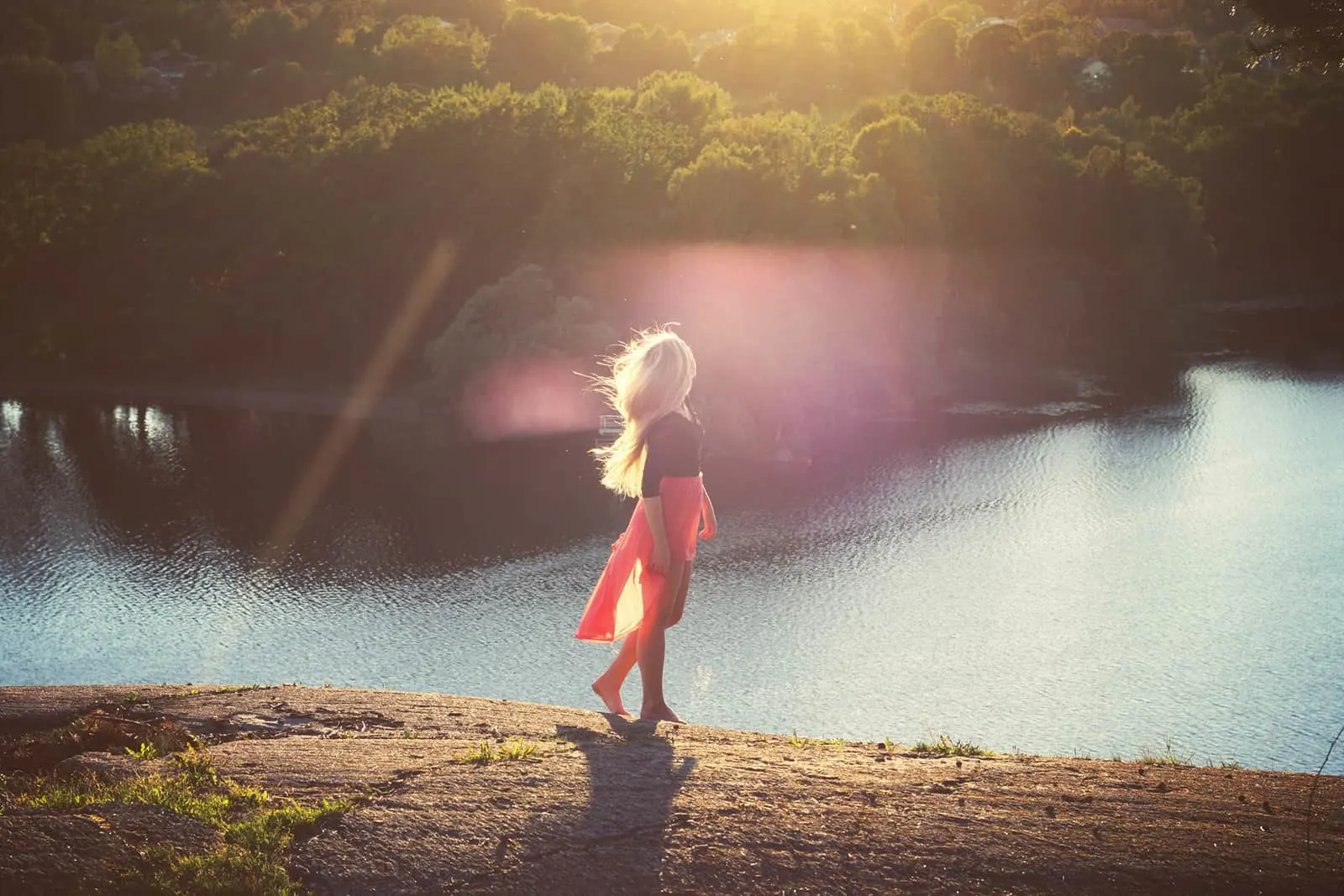 Frau, die allein in der Nähe des Sees während des Sonnenuntergangs geht
