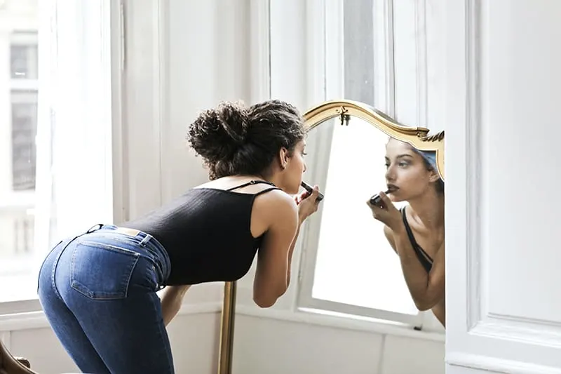 Frau, die Lippenstift vor dem Spiegel aufträgt