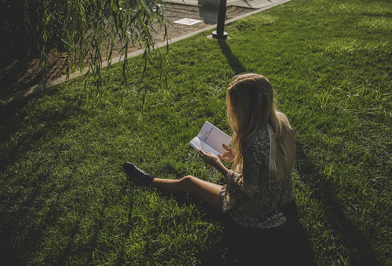 Frau, die ein Buch liest, während sie auf dem Gras sitzt