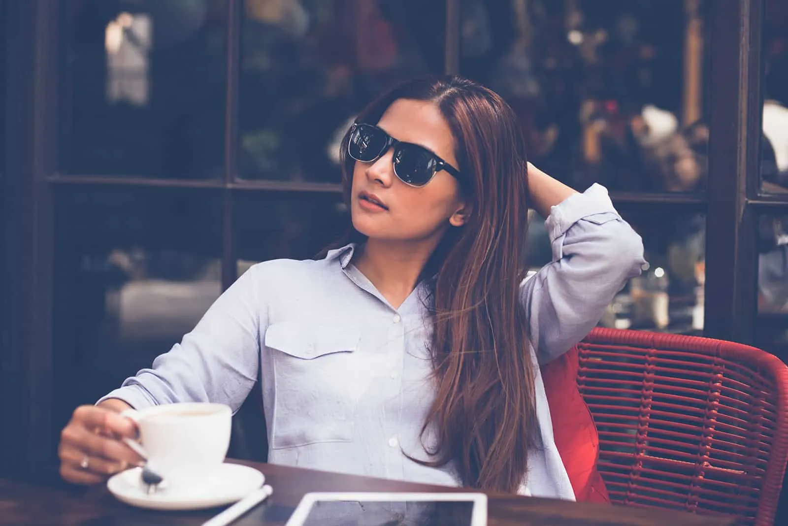Frau mit Sonnenbrille sitzt Kaffee allein im Café trinkend