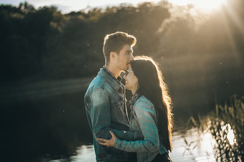 Mann, der eine lächelnde Frau auf einer Stirn küsst, während er auf einem Sonnenuntergang steht