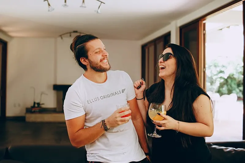 Mann und Frau lachen zusammen, während sie Getränke im Haus halten