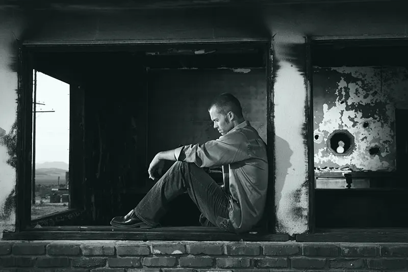 depressiver Mann sitzt auf der Fensterbank eines alten Gebäudes