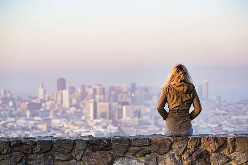 Die Frau sitzt auf der Felsplattform und betrachtet eine Stadt