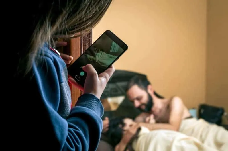 ein Mädchen, das mit seinem Handy ein Foto von einem Mann im Bett macht