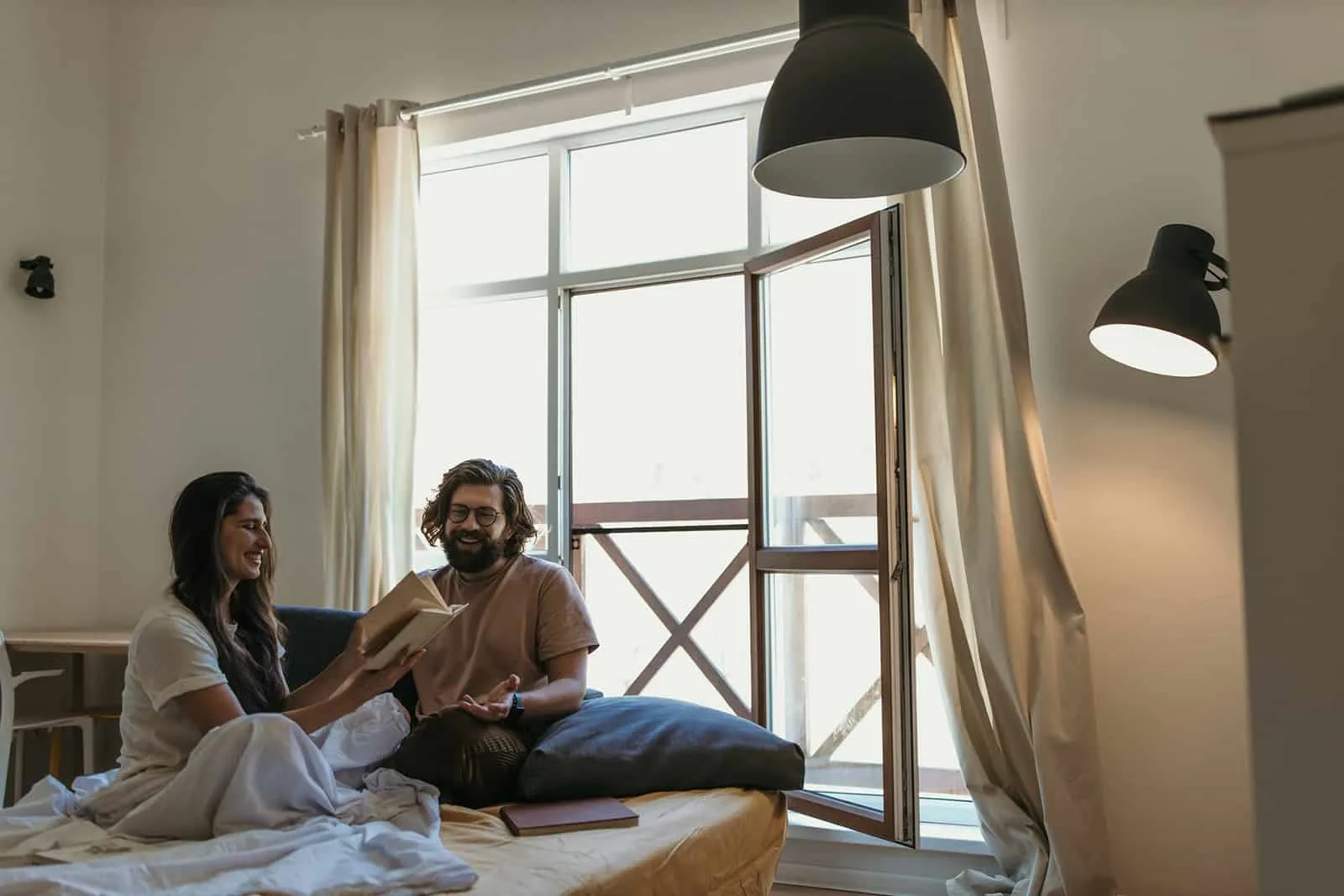 ein lachendes Paar sitzt auf dem Bett und liest ein Buch