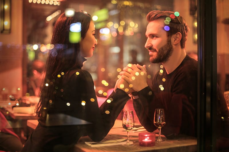 ein liebevolles Paar Händchen haltend in einem romantischen Restaurant sitzen