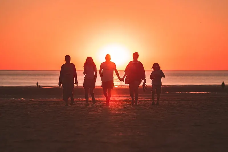 eine Familie, die während des Sonnenuntergangs am Strand spazieren geht