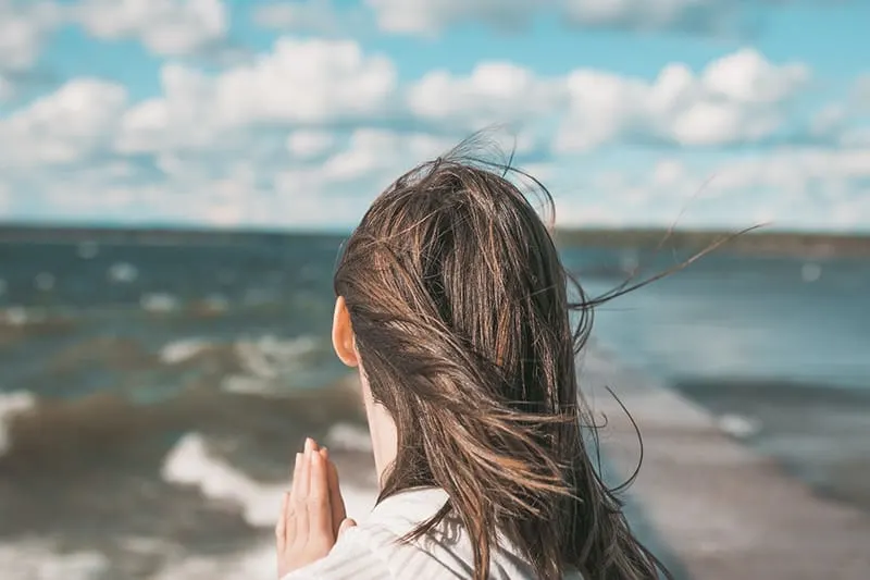Eine Frau, die dankbar ist und sich ihren Handflächen anschließt, während sie auf den Ozean blickt